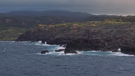 Aerial-view-of-jagged-rocks-along-the-coast-of-Maui-Hawaii-with-the-sun-low-and-cloudy-sky