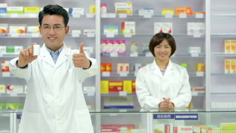 Farmacéutico-Masculino-Sonriendo-Sosteniendo-Un-Frasco-De-Medicina-De-Tableta-Digital-Y-Recomendando-Pastillas-Médicas-En-Una-Farmacia