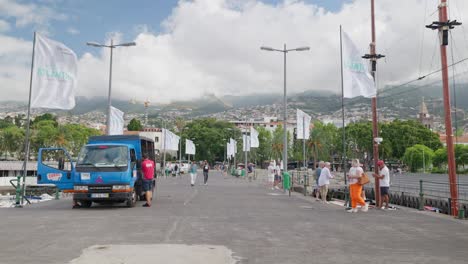 Gente-Caminando-Y-Relajándose-En-El-Puerto-De-Funchal-Con-Montañas-Al-Fondo