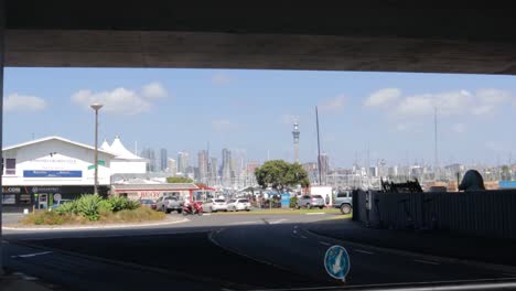 Eine-Kamerafahrt-Unter-Einer-Brücke-Mit-Der-Skyline-Von-Auckland-Im-Hintergrund-An-Einem-Sonnigen-Nachmittag-Mit-Blauem-Himmel-In-Neuseeland