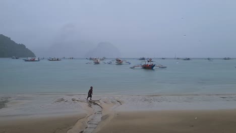 Niño-Divirtiéndose-En-La-Arena-Mojada-Y-La-Playa-En-Un-Día-Lluvioso-En-El-Nido,-Isla-De-Palawan,-Filipinas