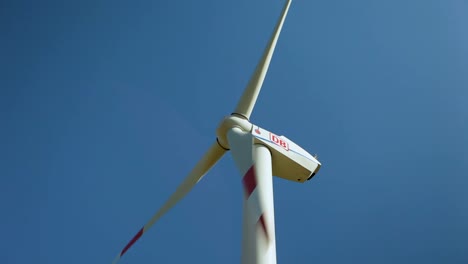 White-wind-turbine-with-red-tips-spinning-against-a-clear-blue-sky,-symbolizing-renewable-energy