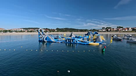 huge-gymkhana-floating-on-the-water-with-the-beach-and-housing-buildings-for-rent-to-tourists-in-the-background,-sunny-summer-morning,-shot-traveling-to-the-left