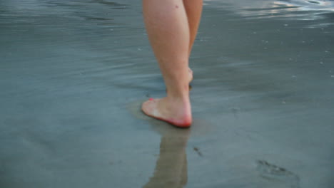 Feet-Walking-on-Dark,-Reflective-Beach-at-Dusk-Over-Waves-in-Slow-Motion