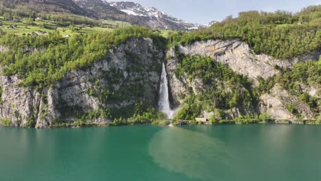 Aerial-view-of-Seerenbach-Falls-cascading-into-turquoise-Walensee,-surrounded-by-lush-cliffs