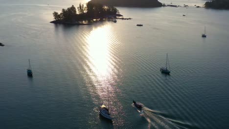 Atemberaubende-Luftaufnahmen-Von-Langkawi,-Malaysia,-Die-Glühende-Sonne-Versinkt-Hinter-Dem-Horizont,-Ein-Segelboot-Gleitet-über-Ruhiges,-Im-Goldenen-Sonnenlicht-Schimmerndes-Wasser,-Ein-Tropisches-Paradies-Entfaltet-Sich