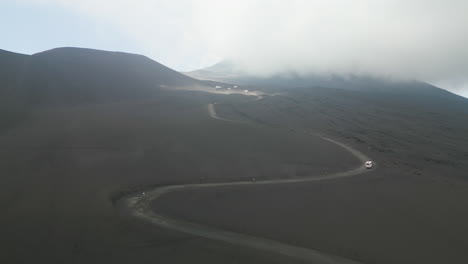 Panoramic-aerial-dolly-rises-above-winding-dirt-road-as-trekking-tour-drives-along-switchbacks-up-volcano