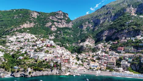 Vista-Aérea-Lateral-Sobre-La-Playa-De-Positano-Rodeada-De-Altas-Montañas,-Exuberante-Vegetación,-Aguas-Turquesas-Y-Hermosas-Casas-Costeras,-Costa-De-Amalfi,-Región-De-Campania,-Italia,-Europa