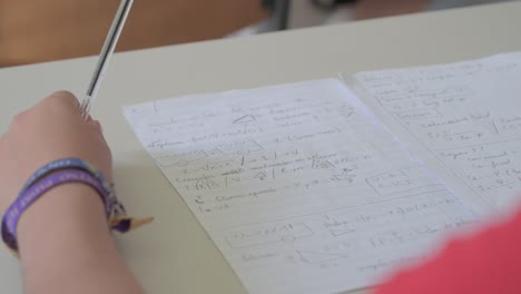 Student's-hand-holding-a-blue-pen-over-electricity-class-notes-on-a-desk