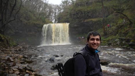 Man-puffing-due-to-the-strong-rain-in-Sgwd-Yr-Eira-Waterfall,-Wales