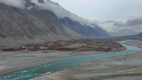 Serene-mountain-village-along-a-vibrant-blue-river-in-Nomal,-Gilgit-Baltistan