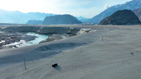 Off-road-vehicle-traversing-Sarfaranga-Cold-Desert's-sandy-terrain-with-snow-capped-mountains-in-the-background