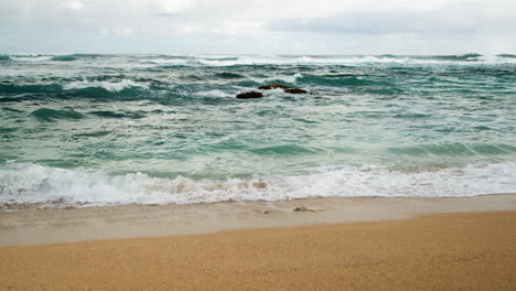 Aufgewühlte-Blaugrüne-Wellen-An-Einem-Stimmungsvollen-Strand-In-Zeitlupe