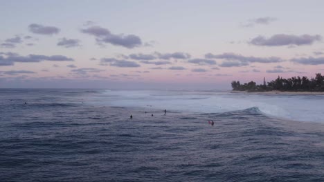 Surfers-enjoy-the-evening-waves-under-a-pastel-sky-at-North-Shore,-Oahu