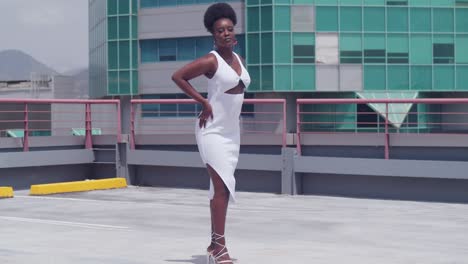 Una-Chica-Negra-Con-Un-Vestido-Blanco-En-Una-Azotea,-Con-El-Horizonte-De-La-Ciudad-A-La-Vista.