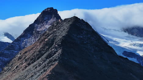 Christian-Catholic-religious-Jesus-Christ-Cross-rocky-glacier-mountain-top-drone-aerial-Saas-Fee-Swiss-Alps-Switzerland-fall-autumn-sunny-blue-sky-mid-day-cloudy-layer-forward-reveal-pan-up-motion