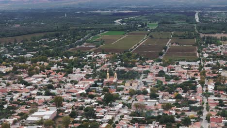 Toma-Aérea-De-Un-Dron-De-La-Ciudad-De-Cafayate-Salta-En-Argentina-Con-Una-Granja-De-Viñedos-Al-Fondo