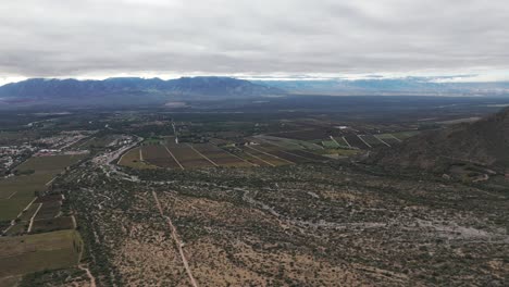 Aerial-drone-shot-of-vineyard-farms-with-Andean-Cordillera-Mountain-Range-in-cafayate-salta-of-Argentina-south-america