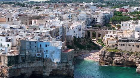 Seitliche-Luftaufnahme-Des-Strandes-Lama-Monachile-Mit-Der-Stadt-Polignano-A-Mare-Im-Hintergrund,-Italien