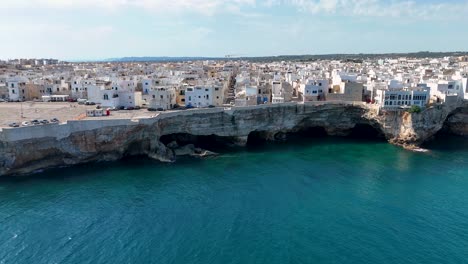 Side-Aerial-View-Of-Polignano-A-Mare-Town-At-The-Edge-Of-A-Rugged-Cliff-In-Puglia,-Italy,-Adriatic-Sea