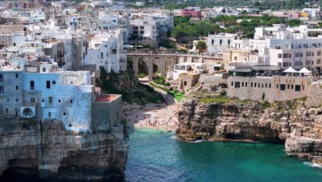 Slow-Aerial-Reveal-Of-Lama-Monachile-Beach-Surrounded-By-Polignano-A-Mare-Cliff-Town,-Italy