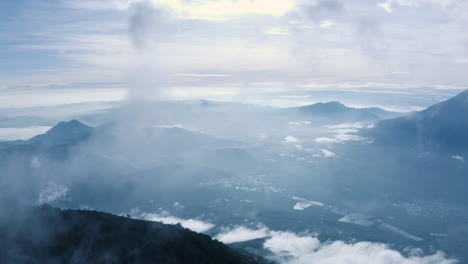 Luftaufnahme-über-Epische-Vulkanlandschaft-Mit-Wolken,-Die-In-Dünnen-Ranken-In-Den-Blauen-Himmel-Von-Guatemala-Aufsteigen