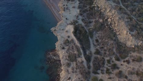 Aerial-drone-shot-captures-the-stunning-cliffs-and-blue-ocean-at-Es-Bol-Nou-beach,-with-a-few-people-enjoying-the-scenic-coastal-setting