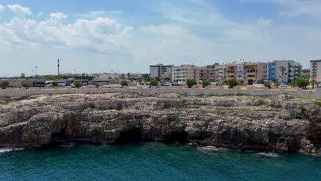 Vista-Aérea-Lateral-De-Un-Acantilado-Escarpado-Frente-Al-Mar,-Agua-Turquesa,-En-Polignano-A-Mare,-Italia