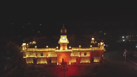 Toma-Aérea-De-Un-Dron-De-Un-Edificio-Histórico-De-La-Torre-Del-Reloj-Iluminado-Durante-La-Noche-En-La-Ciudad-De-Gwalior-En-Madhya-Pradesh,-India