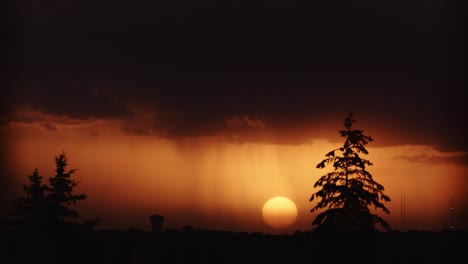 Ein-Zeitraffer-Der-Sonne,-Die-Nach-Einem-Sturm-Am-Horizont-Untergeht,-Mit-Kiefern-Im-Vordergrund