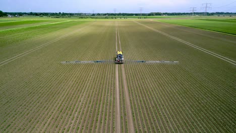 Self-propelled-sprayer-sprays-the-young-crop,-drone-footage-from-the-back