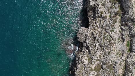 Top-Down-View-Of-A-Rugged-Cliff-Sea-Front,-Turquoise-Water,-In-Polignano-A-Mare,-Italy