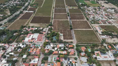 Drohnenaufnahme-Der-Stadt-Cafayate-In-Salta-In-Argentinien-Mit-Der-Andenkordillere-Und-Einem-Weingut-Im-Hintergrund