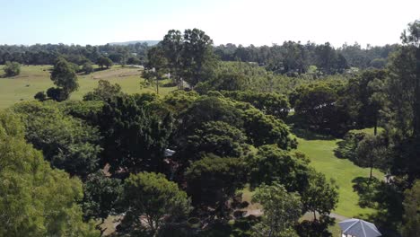 Drone-ascending-over-a-green-park-with-children's-playground-and-a-horse-training-park-in-the-background