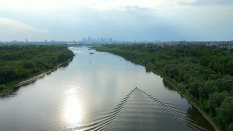 High-above-river-water,-ripple-water-motion,-boat-tracking,-distant-city