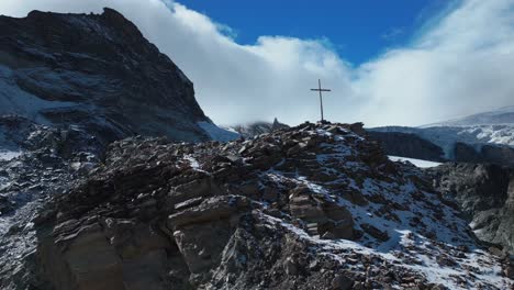 Close-up-Christian-Catholic-religious-Jesus-Christ-Cross-rocky-glacier-mountain-top-drone-aerial-Saas-Fee-Swiss-Alps-Switzerland-fall-autumn-sunny-blue-sky-mid-day-cloudy-layer-circle-right