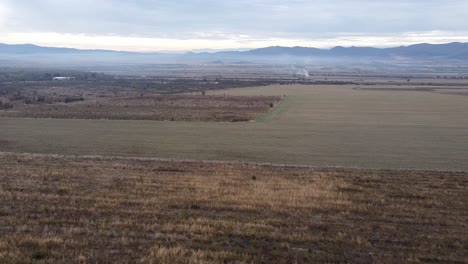 Aerial-footage-of-East-European-farm-fields-in-late-autumn,-a-mountain-in-the-background