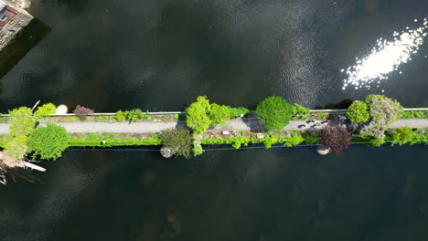 Panoramic-view-of-iconic-footbridge-at-Bridge-of-Flowers,-Shelburne-Falls-with-pristine-river-waters-and-blooming-flowers--aerial-top-down-shot