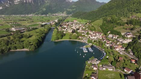 Vista-Aérea-Del-Pintoresco-Lago-Walensee-Y-Su-Zona-Costera,-Con-Un-Pequeño-Puerto-Con-Barcos-Y-Edificios-Residenciales-A-Lo-Largo-De-Las-Orillas,-Que-Encarna-El-Encanto-Del-Encanto-Suizo.