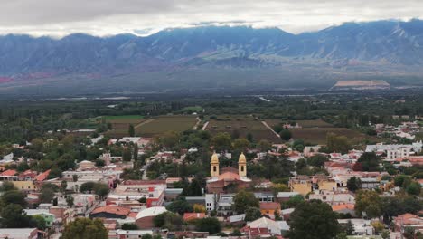 Luftaufnahme-Einer-Drohne-Von-Wohnhäusern-In-Der-Argentinischen-Stadt-Cafayate,-Salta,-Mit-Wolkiger-Bergkette-Im-Hintergrund