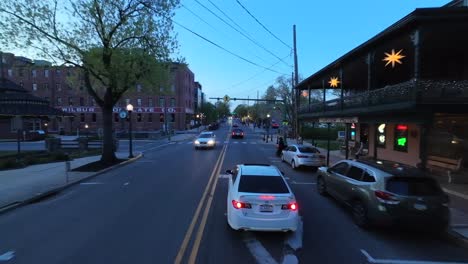 Aerial-FPV-tracking-shot-of-a-white-sedan-driving-through-American-town-at-dusk