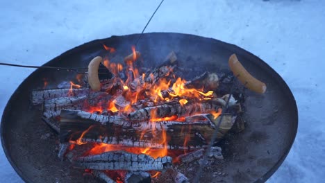 Braten-Von-Würstchen-Am-Spieß-über-Einem-Warmen,-Prasselnden-Feuer,-Gemütliches-Grillen-Im-Winter-Im-Freien