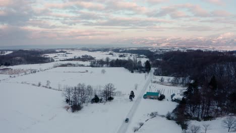 Snow-covered-landscape-in-Iwanai,-Hokkaido,-with-distant-mountains-under-a-pastel-sky,-aerial-view