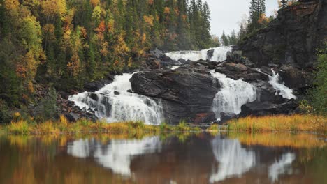 A-mesmerizing-waterfall-cascades-over-dark-cliffs,-its-beauty-mirrored-on-the-serene-surface-of-the-lake-below