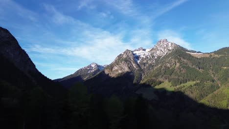 Drone-fly-along-pine-forest-with-Snowy-Mountain-Landscape-in-Background-on-a-sunny-day-in-Austria,-Europe