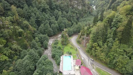 Luftaufnahme-Der-Straße,-Die-An-Der-Naturseite-Vorbeiführt,-Mit-Autos-Und-Lastwagen,-Die-Zwischen-Grünen-Wiesen-Vorbeifahren,-Sonniges-Wetter,-Sonne,-Wetter-Am-Nachmittag