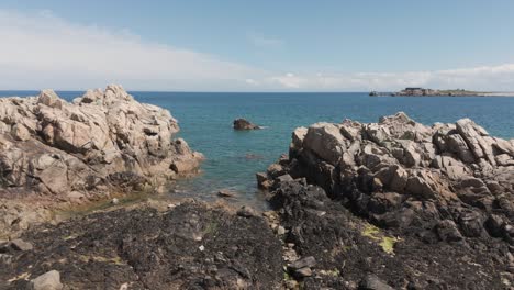 Langsamer-Vorwärtsflug-Mit-Einer-Drohne-über-Eine-Felsige-Bucht-Mit-Kristallklarem-Meer-An-Einem-Ruhigen,-Sonnigen-Tag-In-Guernsey