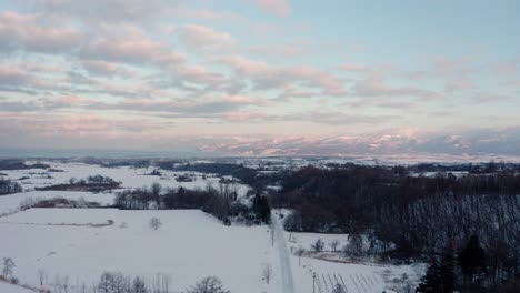 Iwanai,-hokkaido,-showcasing-snowy-fields-and-distant-mountains-at-dawn,-aerial-view