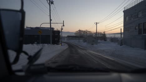 Conduciendo-Por-Las-Calles-Nevadas-De-Iwanai,-Hokkaido-Al-Amanecer,-Con-Cielos-Despejados-De-Invierno-Y-Un-Ambiente-Sereno.