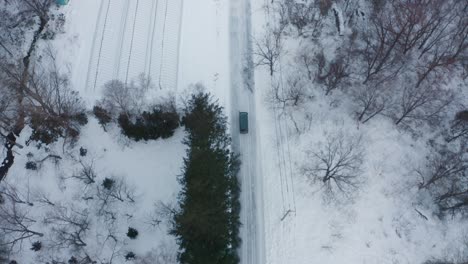 A-car-driving-through-a-snow-covered-forest-road-in-iwanai,-hokkaido,-japan,-aerial-view